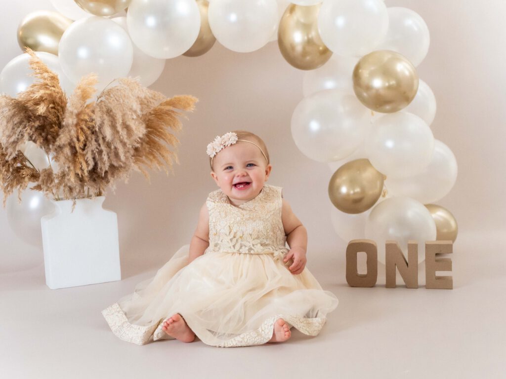 Een vrolijk baby meisje van 1 jaar straalt op de foto omgeven door taartkruimels, haar gezicht en handen bedekt met frosting, terwijl ze lachend en vol vreugde haar eerste verjaardagstaart verkent tijdens een cakesmash shoot in de studio bij van Lente fotografie in Spijkenisse.