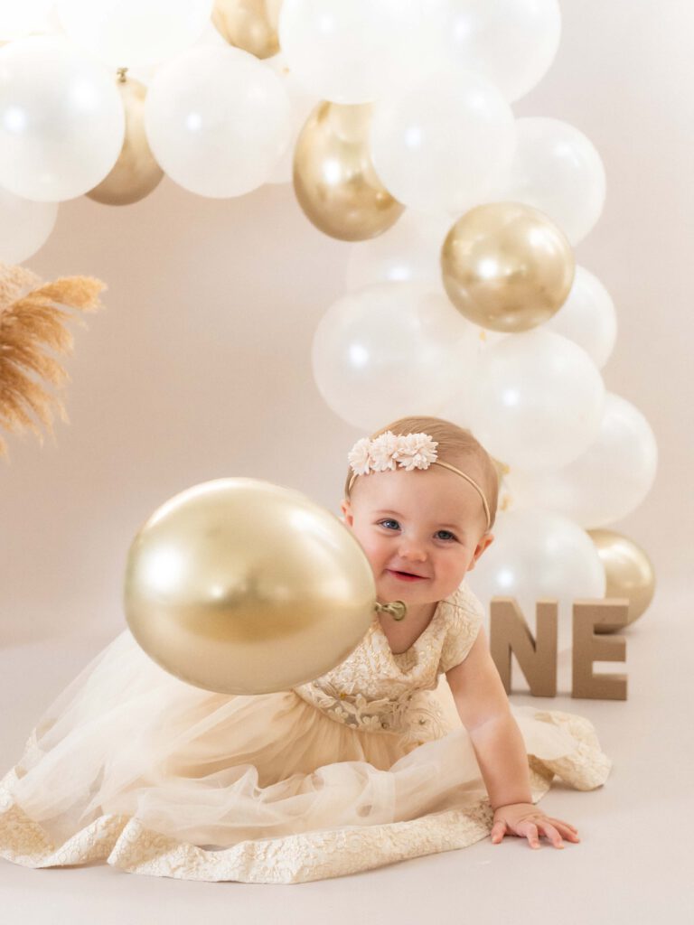 Een vrolijk baby meisje van 1 jaar straalt op de foto omgeven door taartkruimels, haar gezicht en handen bedekt met frosting, terwijl ze lachend en vol vreugde haar eerste verjaardagstaart verkent tijdens een cakesmash shoot in de studio bij van Lente fotografie in Spijkenisse.